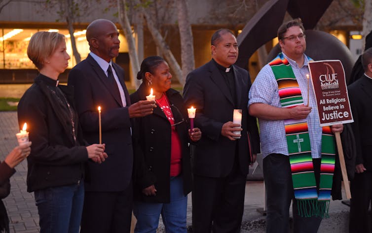 Male and female clergy of different faiths hold candles.