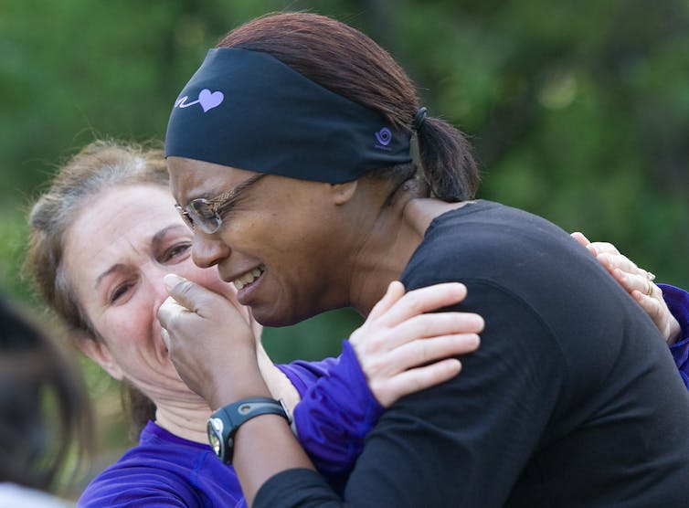 A white woman reaches in to hug a Black woman.