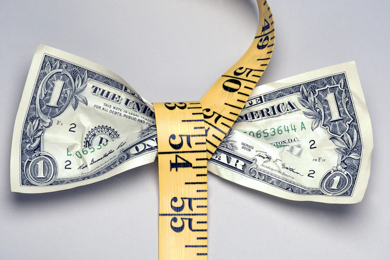 A measuring tape squeezes a dollar bill