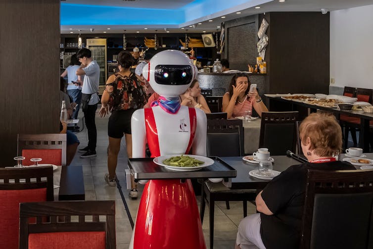 a robot in a red waiter uniform brings a plate to a customer in a cafe