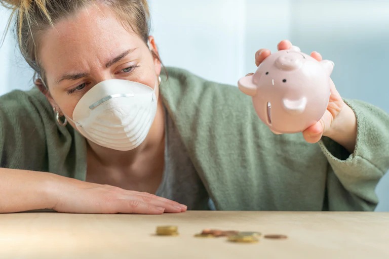 Mujer con mascarilla vacía una hucha de cerdito.