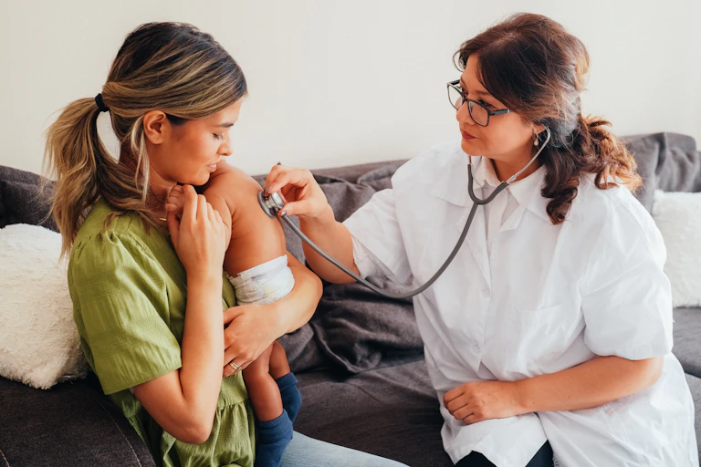 A female doctor performs a checkup on an infant who is being held by its mother.