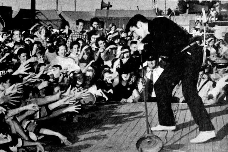 Elvis sings in front of a crowd of fans who reach out to touch him.