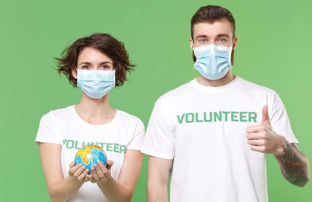 A young woman and young man wearing white T-shirts that read 'Volunteer'; the woman is holding a globe in her hands