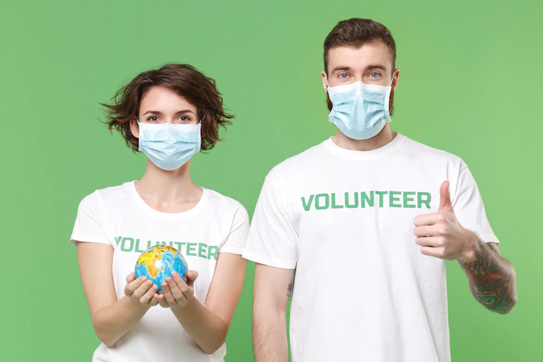 A young woman and young man wearing white T-shirts that read 'Volunteer'; the woman is holding a globe in her hands