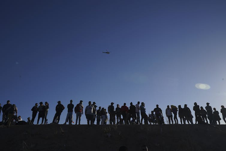 A line of dozens of people are seen standing on a hill.