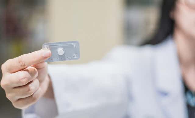 A woman in a white pharmacist's smock holds up the morning after pill.