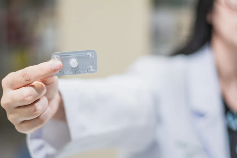 A woman in a white pharmacist's smock holds up the morning after pill.