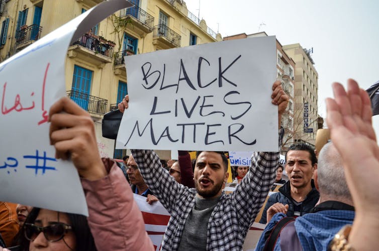 A man holds a sign reading 'Black Lives Matter,' with another sign in Arabic nearby, during a march.