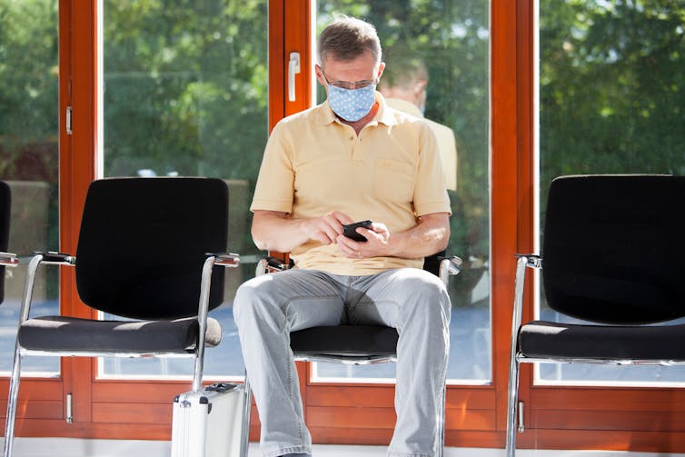 Masked man sits in medical waiting room