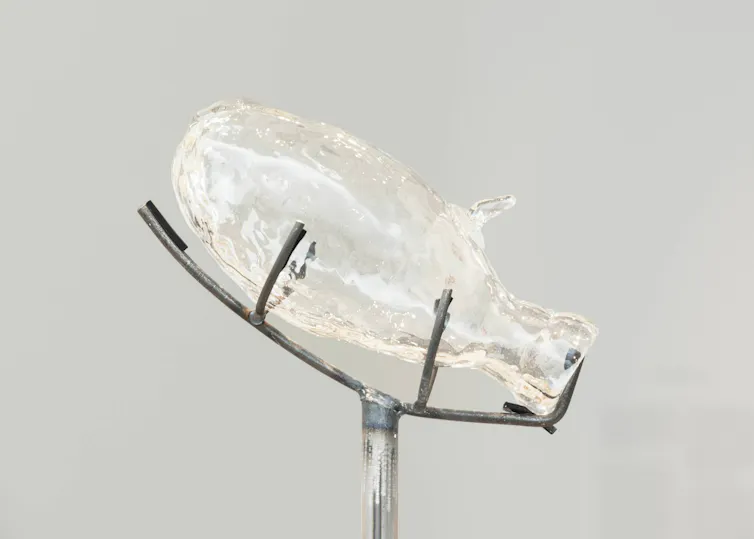 A sculpture resembling a glass bottle held on a metal wire base.