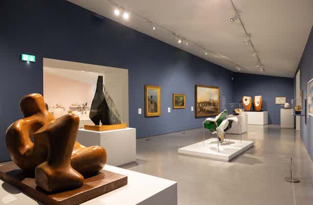 Sculptures and paintings on display in a gallery with blue walls. 