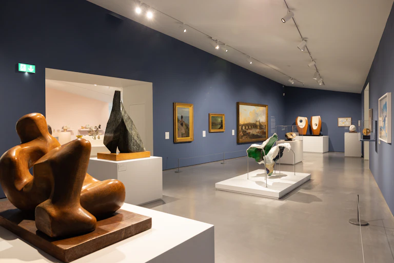 Sculptures and paintings on display in a gallery with blue walls.