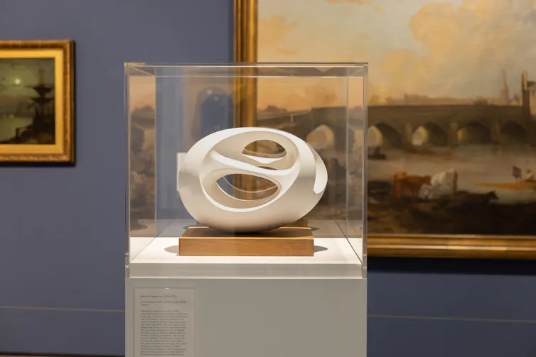 A round white sculpture with holes in the side in a display case.