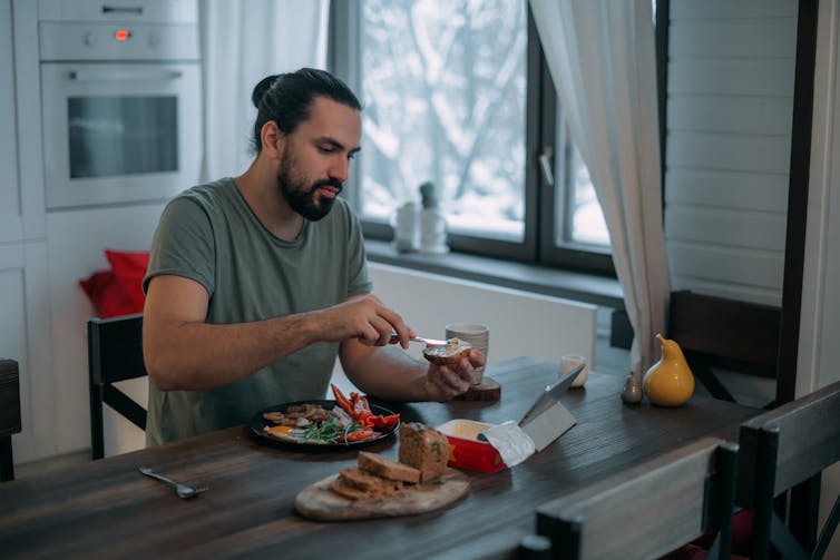 Un joven desayuna abundantemente en la mesa de su cocina.