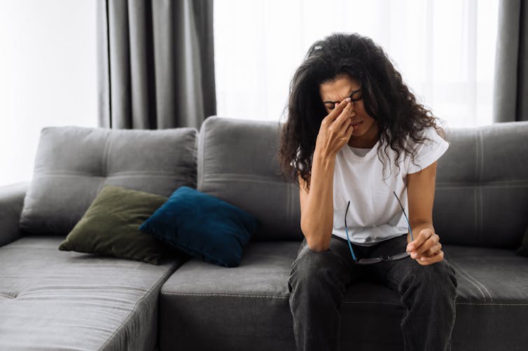 A woman seated on a couch appears stressed.