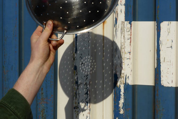 Light from the Sun shines through the holes of a colander and onto a wall, creating many little images of the eclipsed Sun projected onto the wall