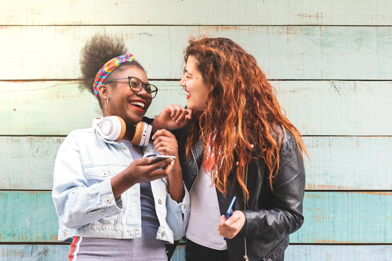 Two girls laugh with their phones.