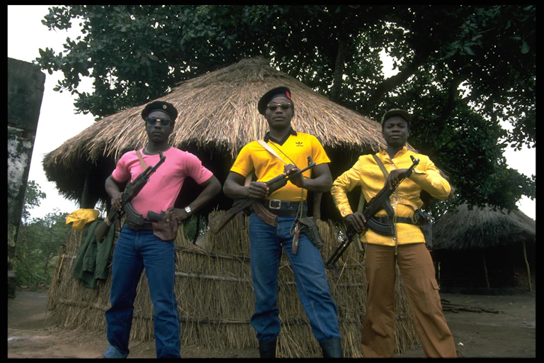 Men stand holding their weapons, wearing sunglasses and berets