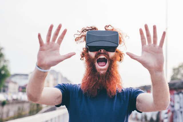 A guy with curly red hair and bushy beard wearing a VR headset in a state of wonder.