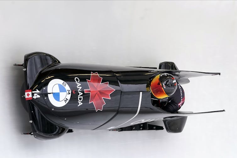 A black bobsleigh on the ice with a red maple leaf and the word Canada on it.