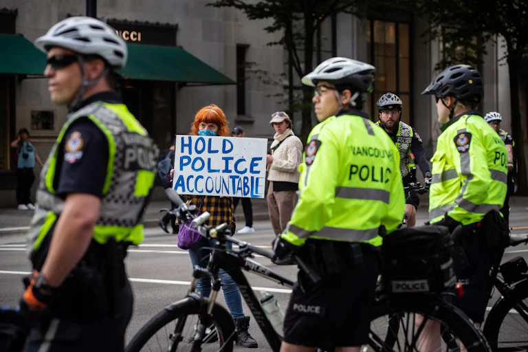 A woman standing near police officers holds a sign that reads: hold police accountable.