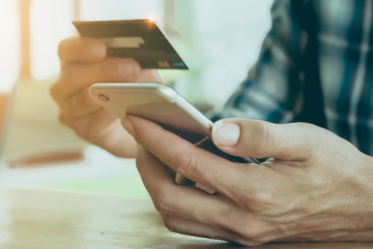 Close up photo of a man's hands holding a mobile phone in one hand and a credit card in the other