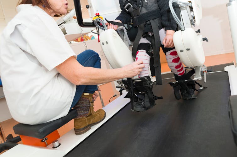 Physical therapist monitoring young patient walking on treadmill with robotic assistance