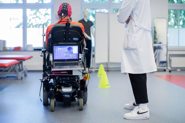 Person in wheelchair uses brain-computer interface to steer with a researcher looking on