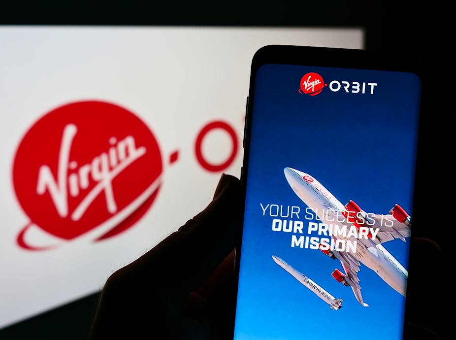  Person holding smartphone with website of American aerospace company Virgin Orbit LLC on screen in front of logo.