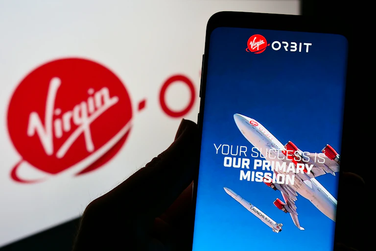 Person holding smartphone with website of American aerospace company Virgin Orbit LLC on screen in front of logo.