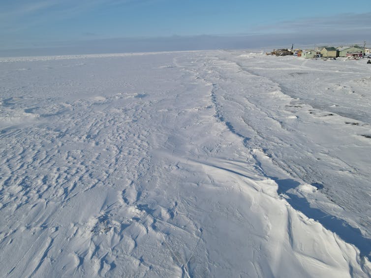 A snow and ice covered ocean with the edge of the island and its homes on one side. It looks cold out.