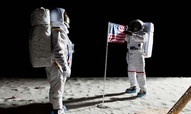 Two astronauts on the surface of the Moon with an American flag.