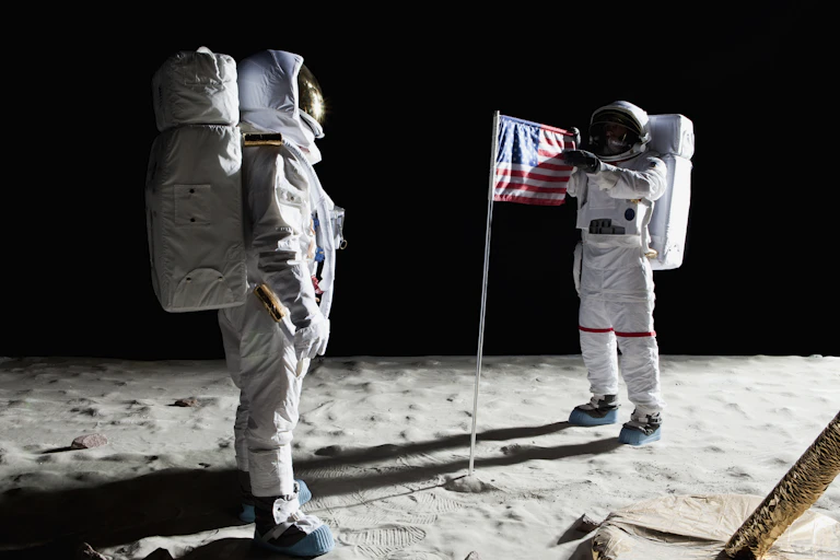 Two astronauts on the surface of the Moon with an American flag.
