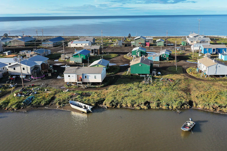 An aerial view of the island in summer showing boats in the bay and clouds out over the ocean. The island is narrow, with about six properties across.