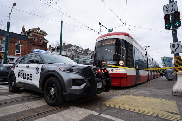 A police van and yellow crime tape are seen beside a red and white streetcar.