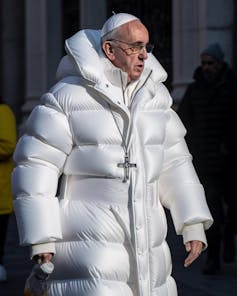 an older white man (the pope) wearing a long white puffer jacket and a white skullcap