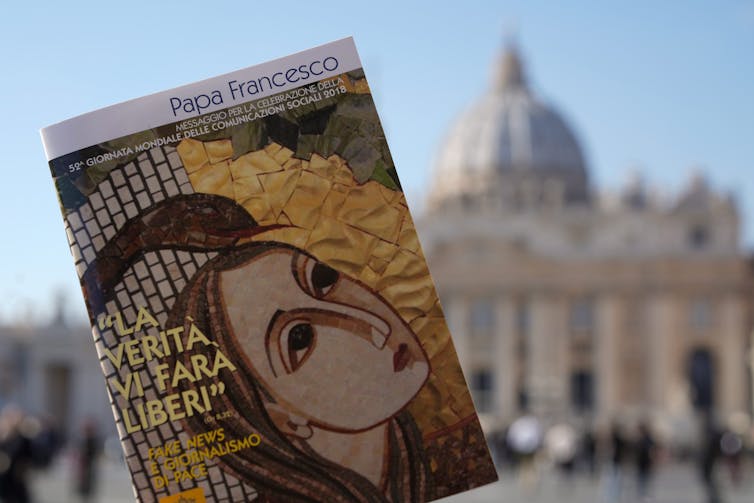 a book is held up with a renaissance style illustration of a woman and a snake on the cover and the words LA VERITÀ VI FARÀ LIBERI