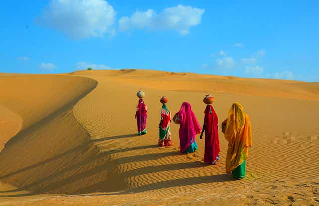 Women walking on a sand dune with pots of water on their head