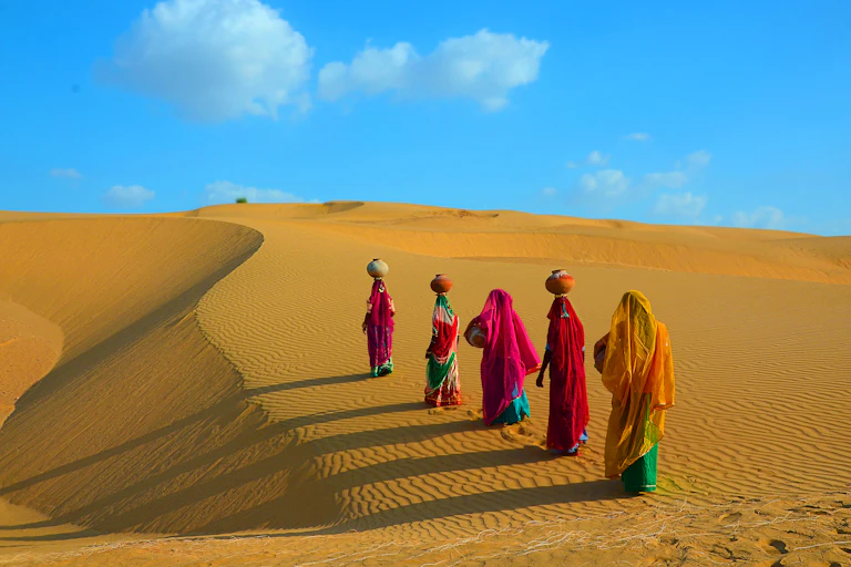 Women walking on a sand dune with pots of water on their head