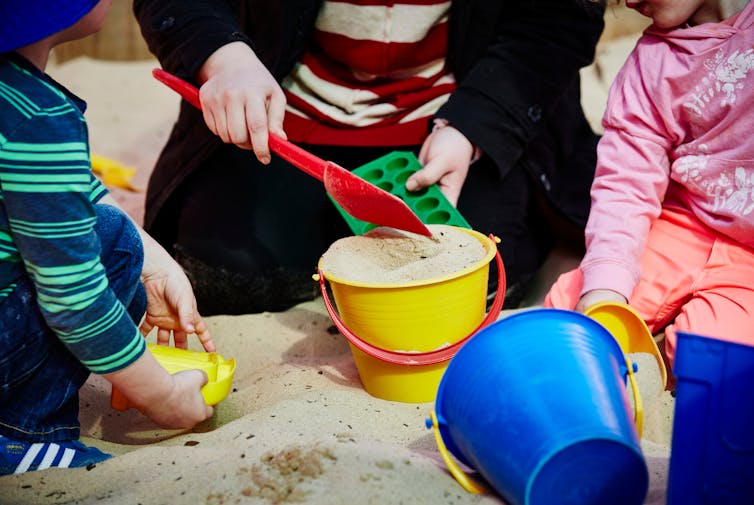 An educator in a sandpit with children and plastic buckets.