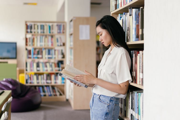 A young woman reads a book in a library.