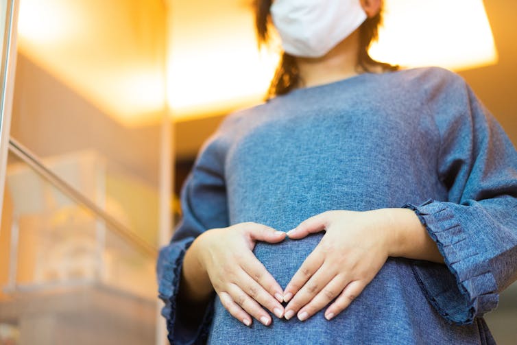 pregnant woman wears masks and puts hands on belly in heart shape