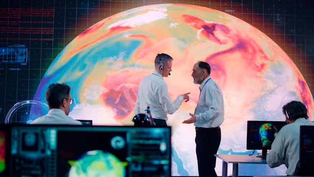 Two men talking in front of large display of temperature on earth