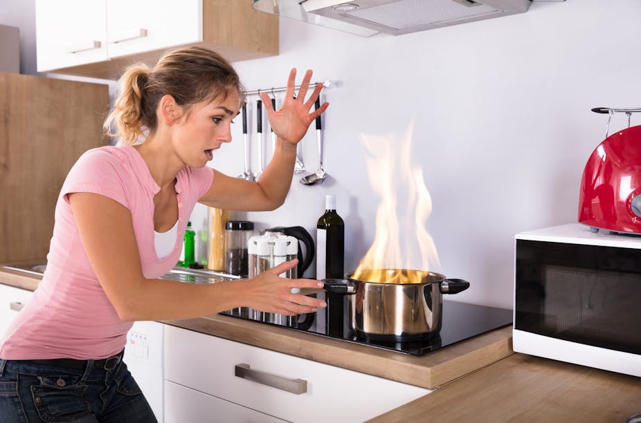 A woman in the kitchen looking at a pan that has caught fire.