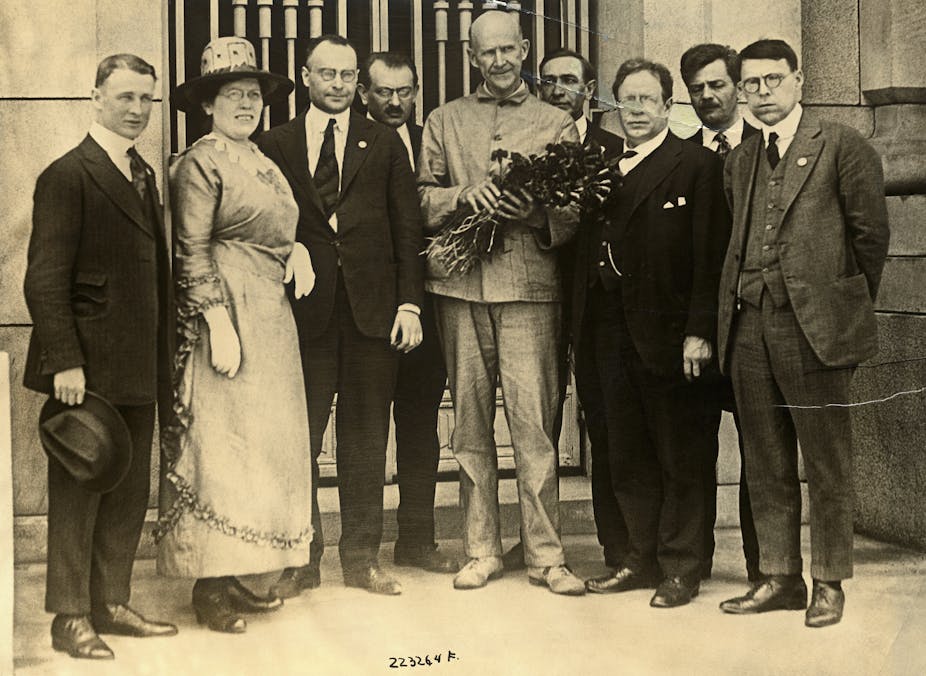 A man holding a bouquet surrounded by men in suits and one woman, standing in front of a building.