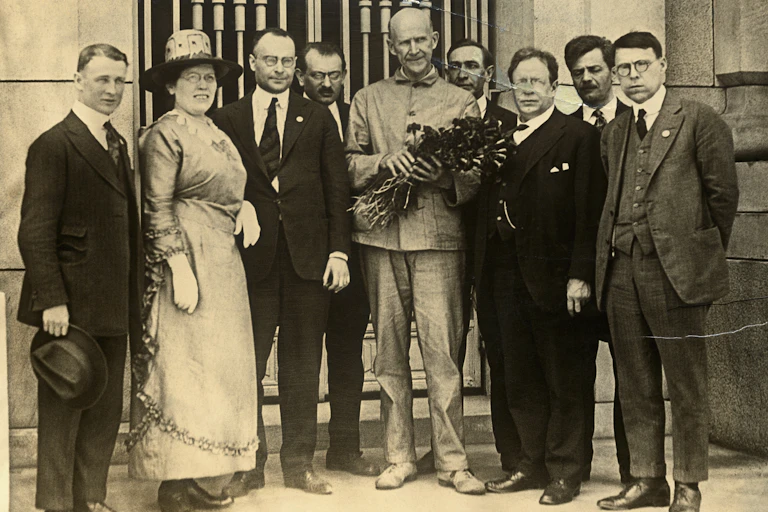 A man holding a bouquet surrounded by men in suits and one woman, standing in front of a building.