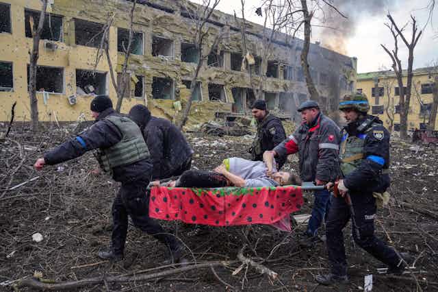 A group of men carry a pregnant woman on a stretcher in Mariupol, Ukraine, March 2022.