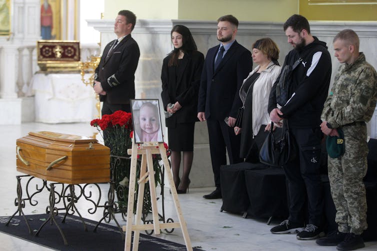Mourners stand by the small coffin of a three-month old child killed in Odesa, Ukraine. By the coffin is a picture of the baby.