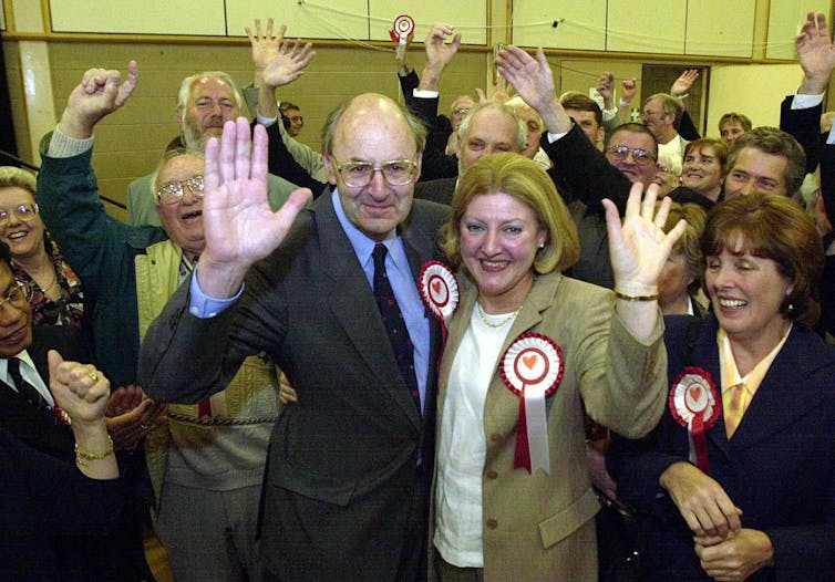 Richard Taylor and his supporters waving at the camera on election night. They are all wearing rosettes.